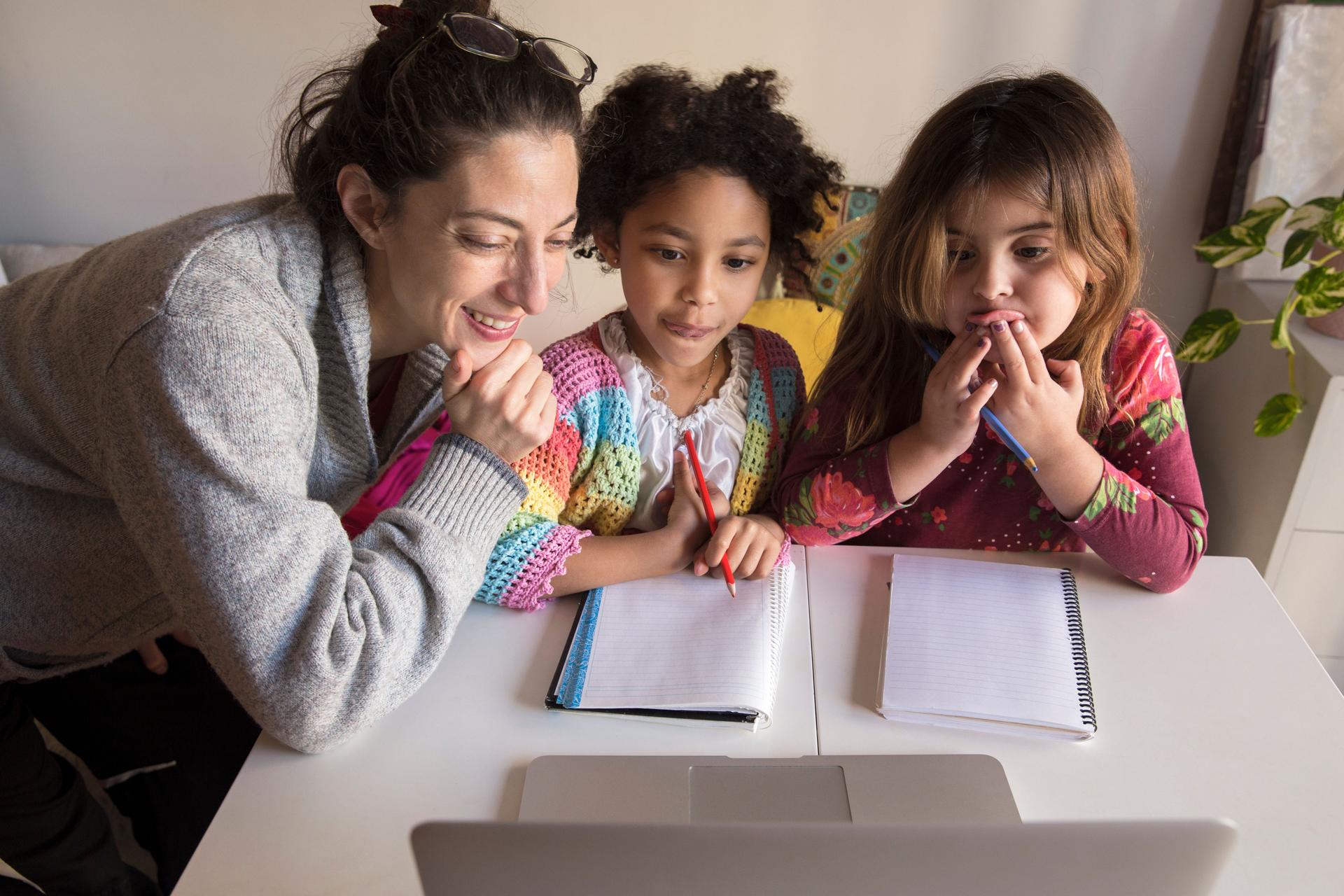 A mother and two children engaged in an online learning session at home, focused on a laptop screen, demonstrating curiosity and excitement