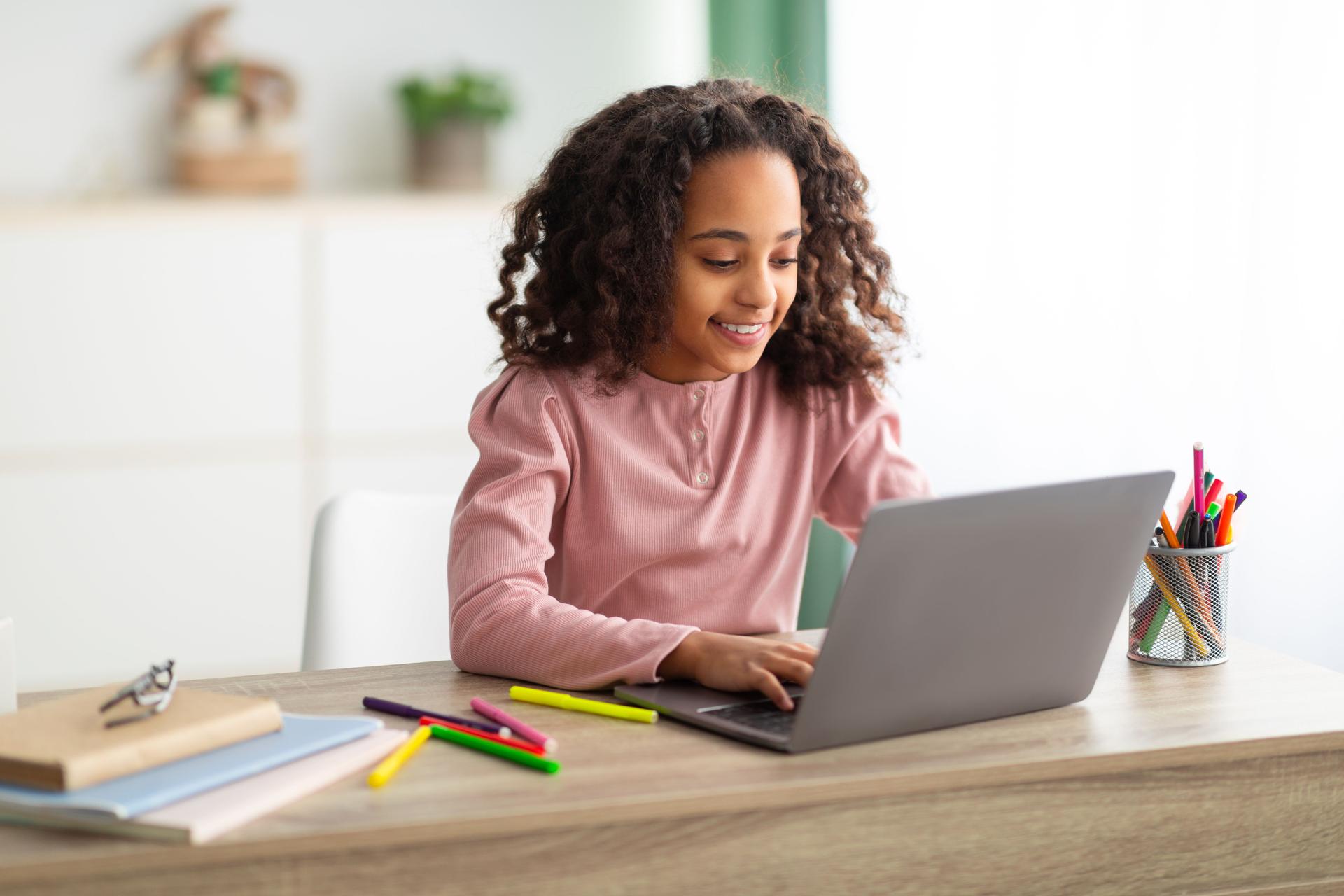 Homeschooling concept. Happy black girl studying at home with laptop, typing on keyboard, sitting in living room